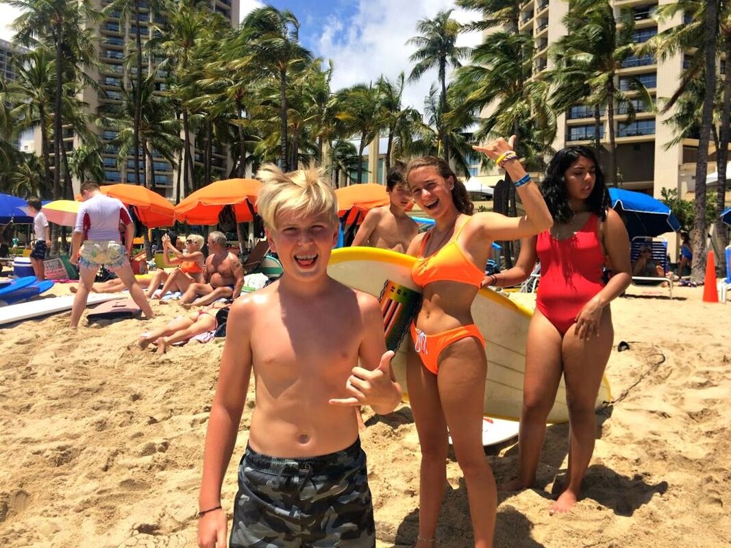 Boy and girls on Waikiki Beach holidng a surfboard giving 