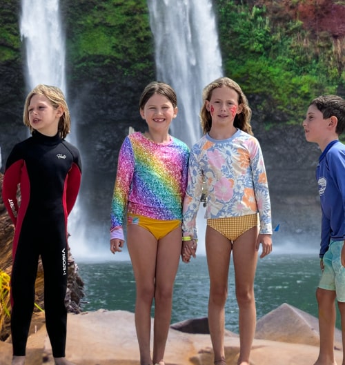Four young campers, two boys and two girls, standing on a rock with a tropical waterfall behind them at Aloha Beach Camp Summer Camp Overnight Camp in Oahu, Hawai