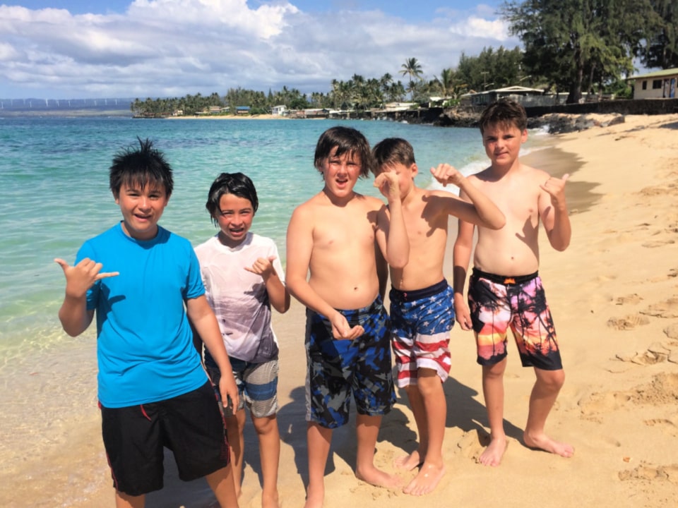 5 boys at summer camp in Hawaii standing on the beach oceanfront and giving the hang loose sign.