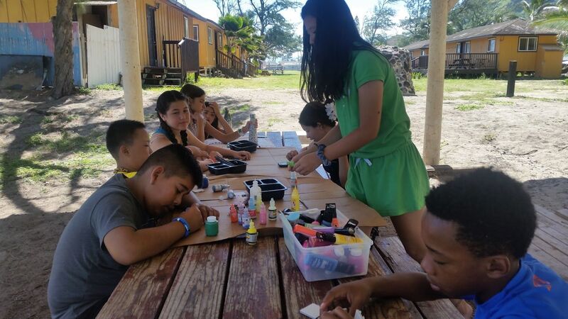 Group of campers doing arts and crafts projects in front of the cabins at Aloha Beach Camp's Hawaii summer camp.