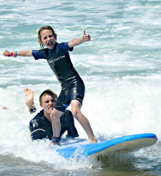 Boy learning to surf with his camp counselor surf instructor at Aloha Beach Camp in Oahu, Hawaii