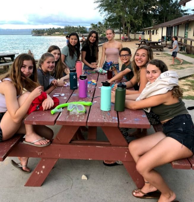 Eight campers and their camp counselor hanging out together in front of their cabin enjoying the ocean view at Aloha Beach Camp's Hawaii summer camp for kids and teens in Oahu, Hawaii.
