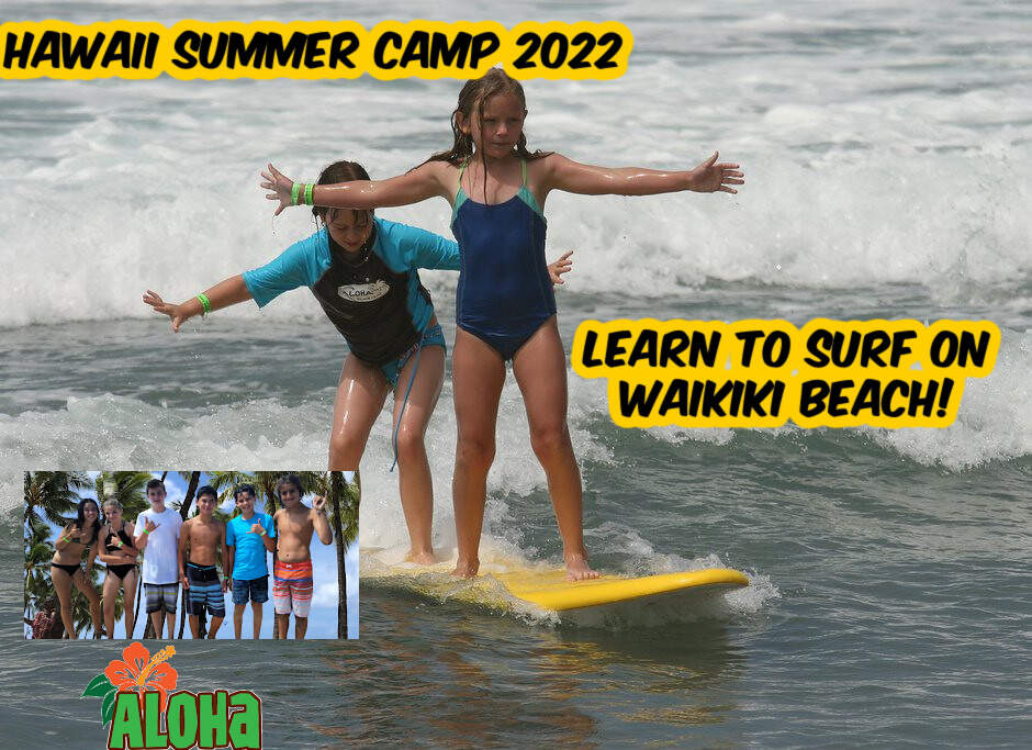 2 girls tandem surfing at Aloha Beach Camp's Hawaii summer camp with other campers looking on giving the 