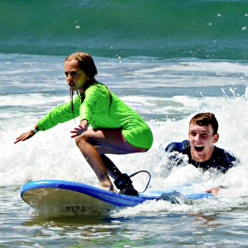 Girl learning to surf with her camp counselor at Waikiki Beach at Aloha Beach Camp's Hawaii summer camp on Oahu.
