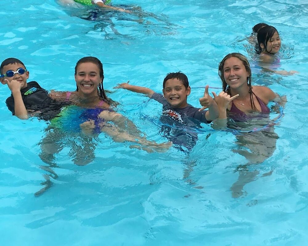 Two female camp counselors and campers enjoying the swimming pool at Aloha Beach Camp's Hawaii summer camp location at Camp Mokuliea on Oahu's North Shore.