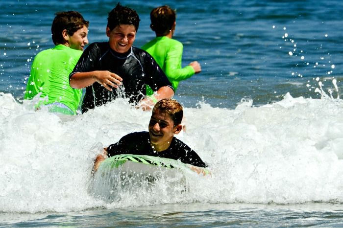 Teenage boy boogie boarding in the ocean with his friends at Aloha Beach Camp's Hawaii summer program for kids and teens.