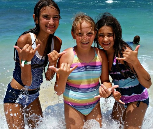 Three girls giving in the ocean giving hang loose sign at Aloha Beach Camp's Aloha Hawaii Sleepaway Summer Camp 2021